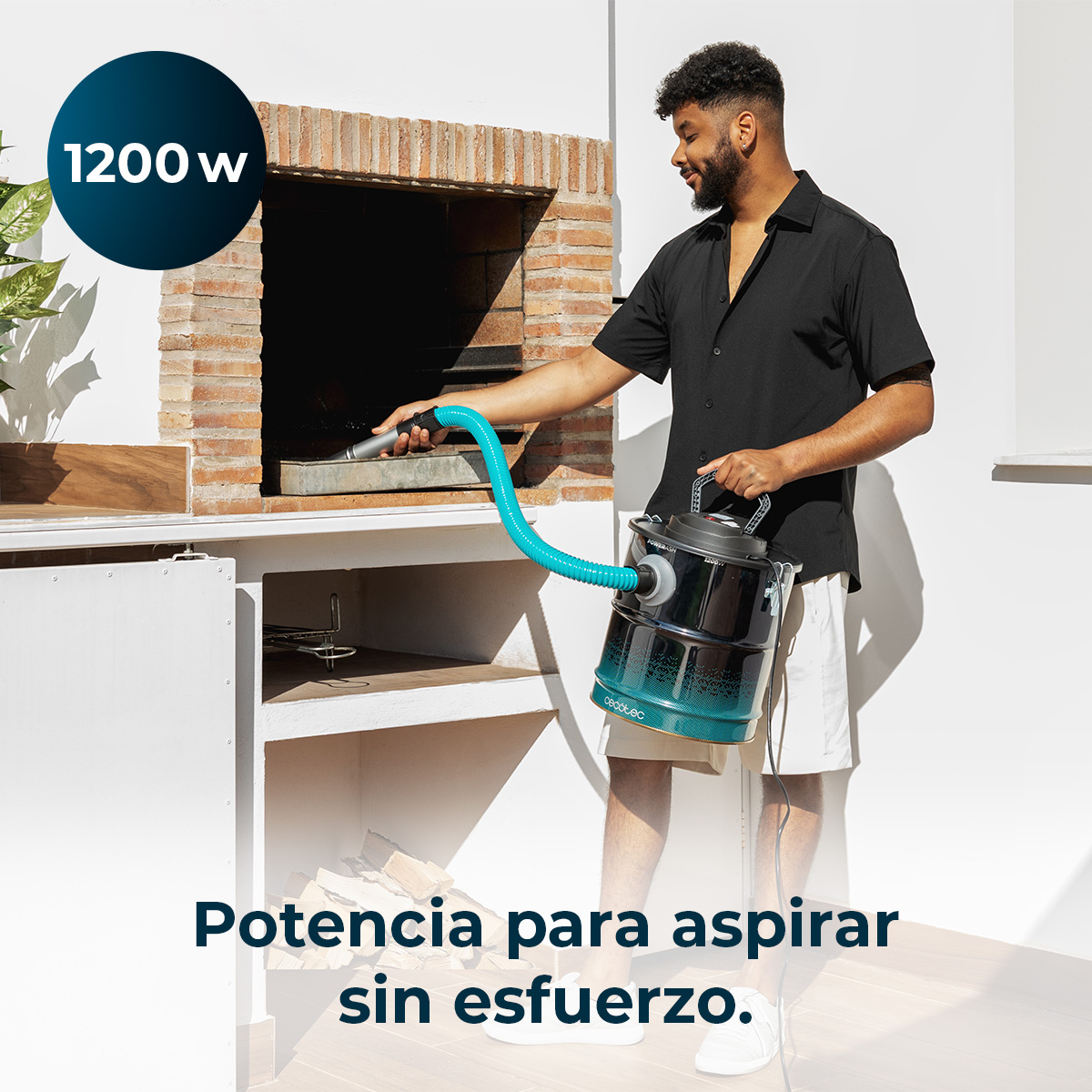 Un uomo usa un aspirapolvere per pulire un barbecue. L'aspirapolvere è collegato da un tubo blu. Sullo sfondo si vede un forno di mattoni.