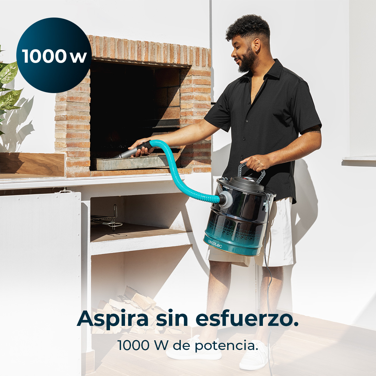 Un uomo aspira una griglia per barbecue. Tiene un aspirapolvere con un tubo verde acqua, con una camicia nera e pantaloncini.