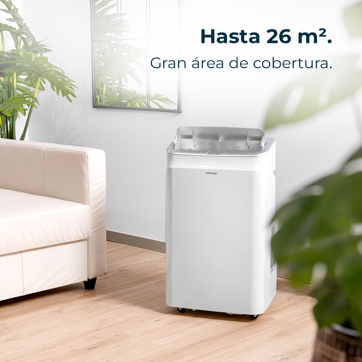 Biały klimatyzator z hiszpańskim tekstem, 'Hasta 26 m2. Gran área de cobertura.' Wnętrze z roślinami i sofą.