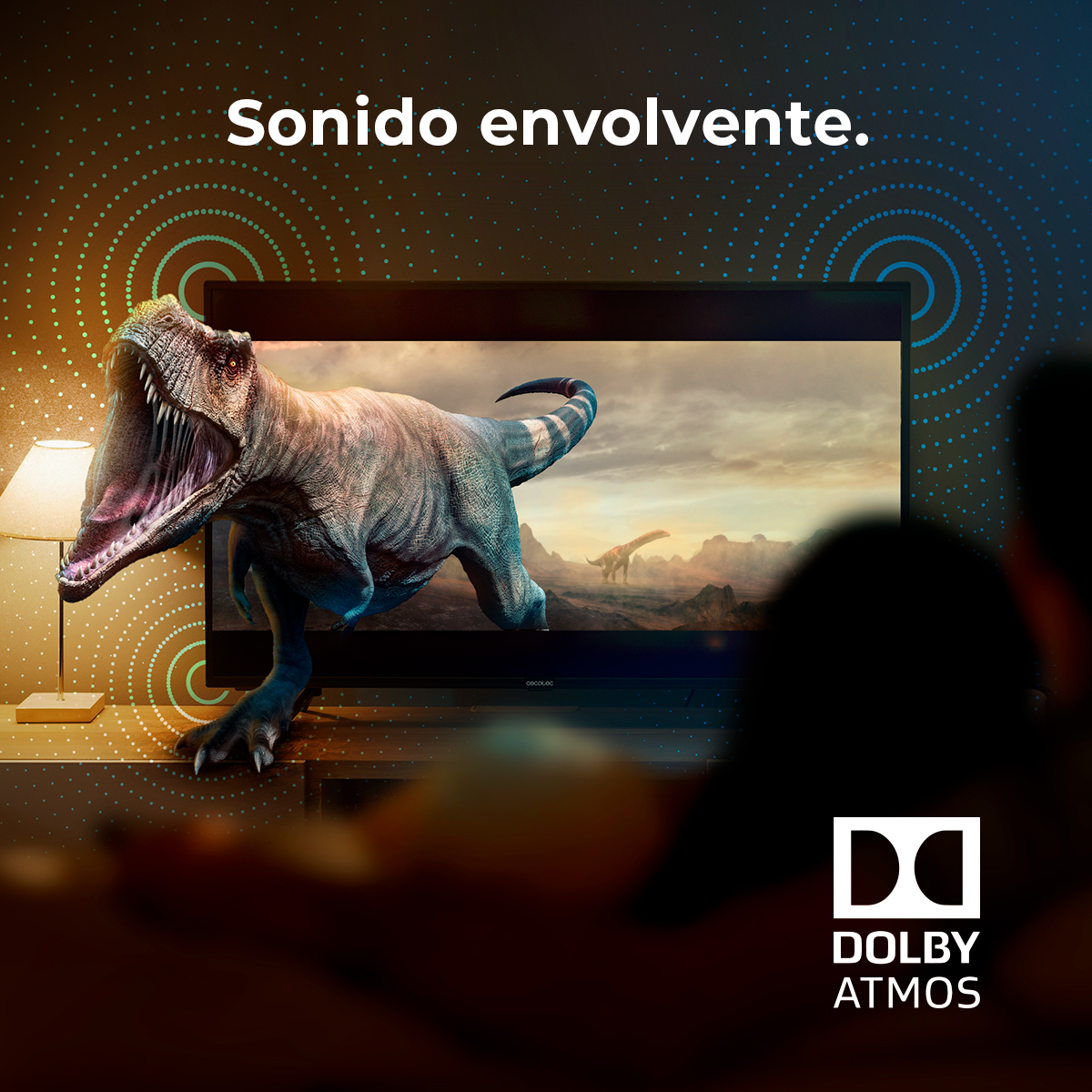 Telewizor wyświetla scenę z dinozaurami. Po lewej lampa. Logo Dolby Atmos po prawej. Ludzie oglądają.