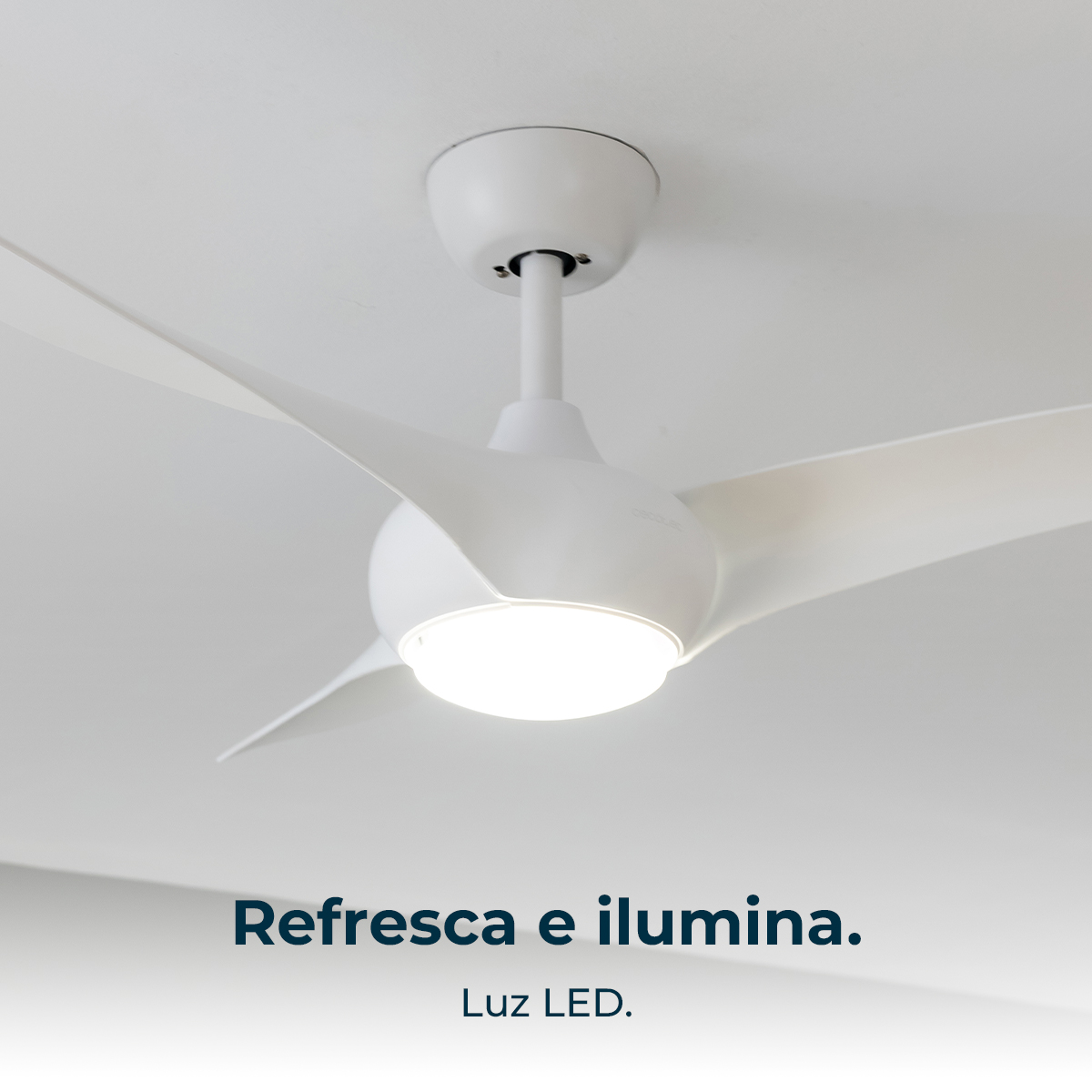 Un ventilatore da soffitto bianco con tre pale e una luce centrale. Il ventilatore è montato su un soffitto bianco. Il testo dice 'Refresca e ilumina'.