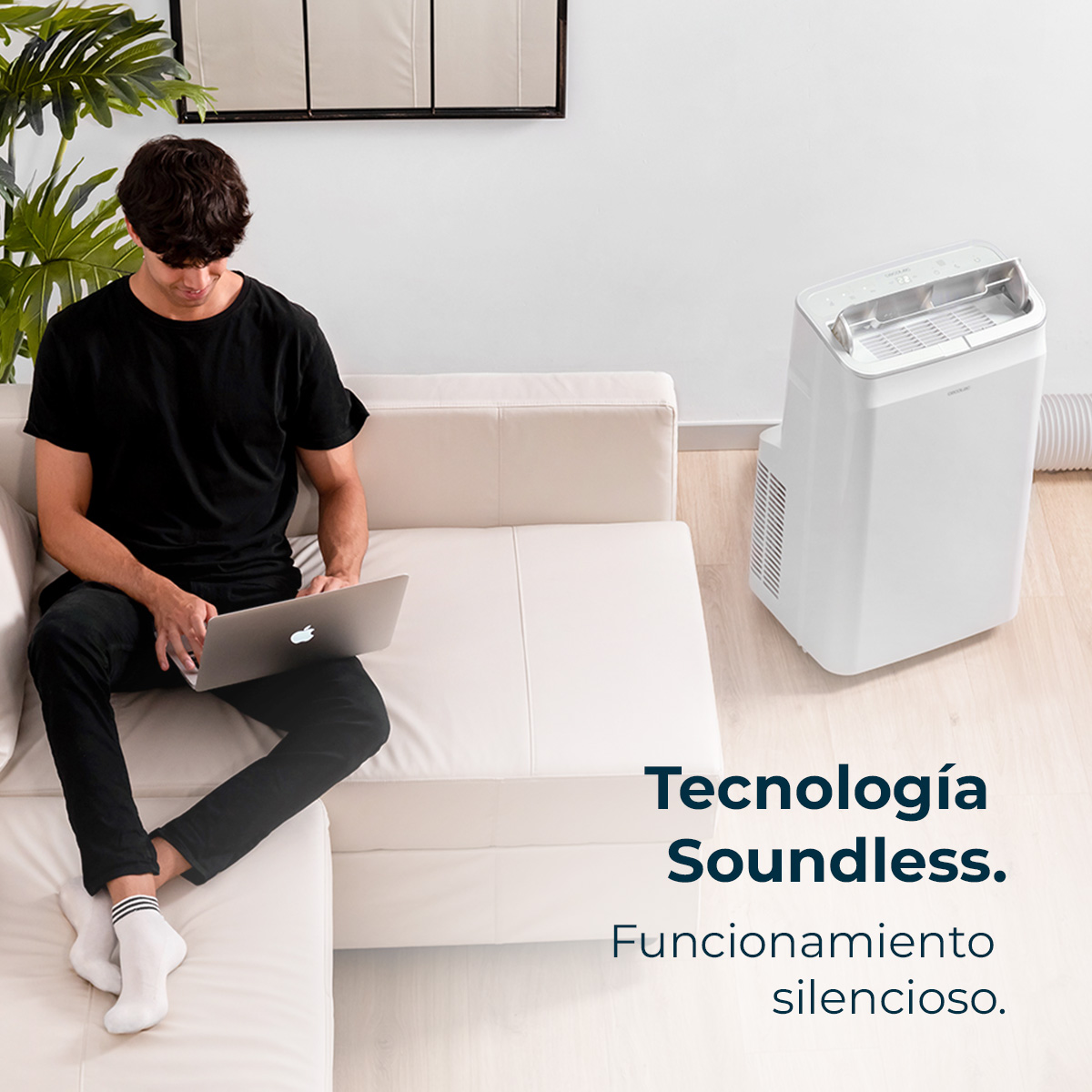 Mężczyzna siedzi na białej sofie, używając laptopa. Obok niego biały klimatyzator. Tekst: 'Technologia Soundless'.