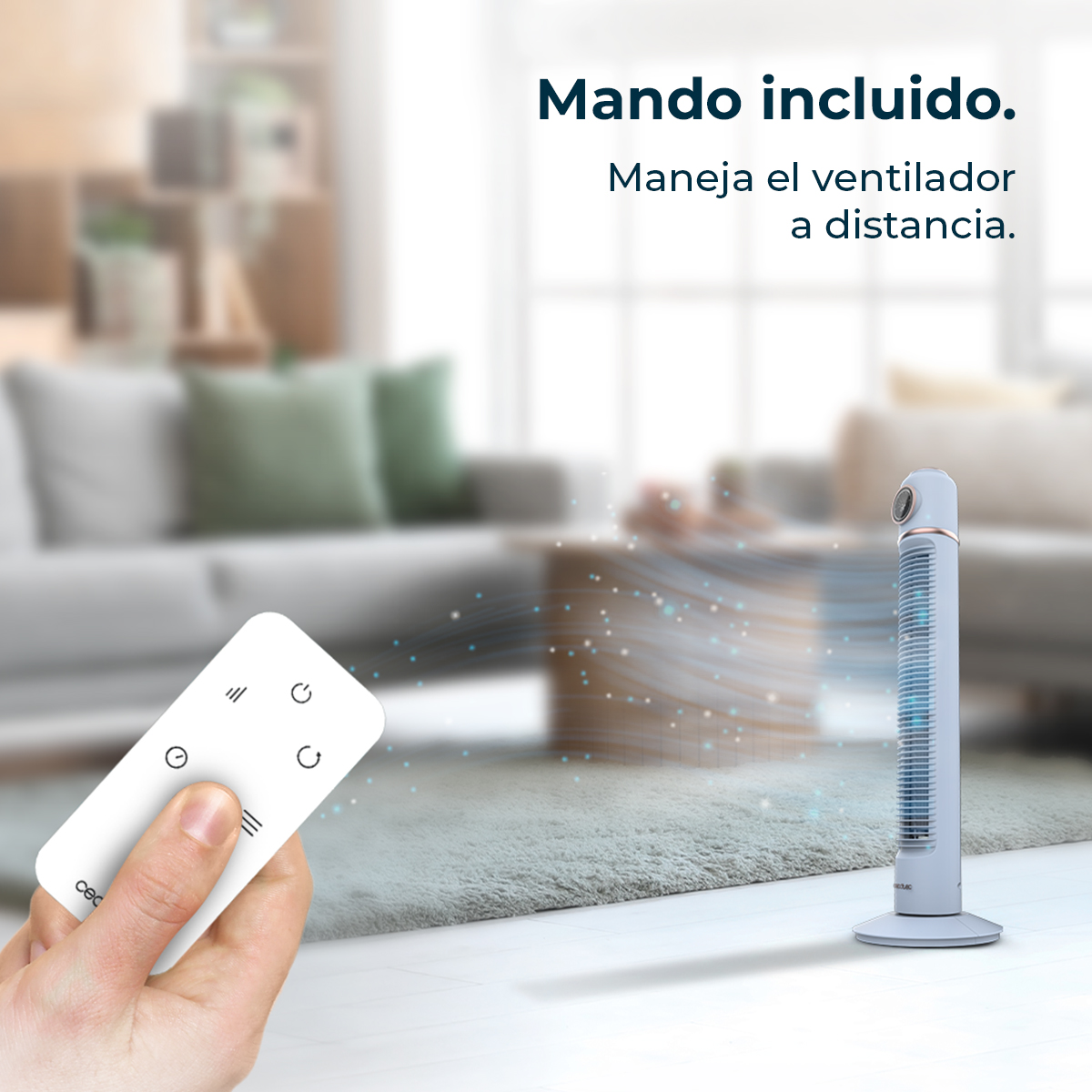 A hand holds a white remote control. A tower fan stands on a carpet. The background shows a living room with a sofa.
