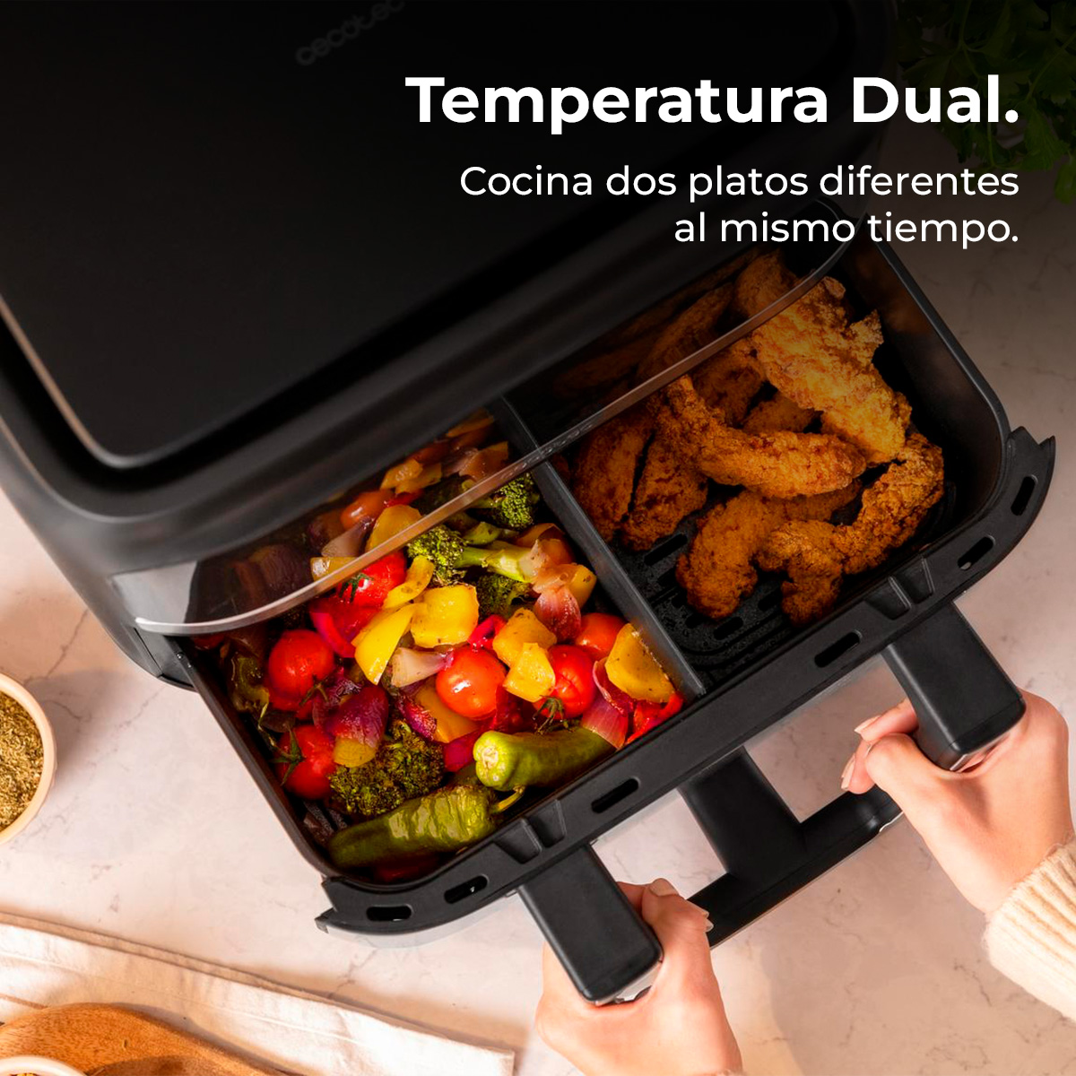 Zwarte airfryer met groenten en gefrituurd voedsel. Handen houden de airfryer vast. Tekst: Dubbele temperatuur, kook twee gerechten tegelijk.