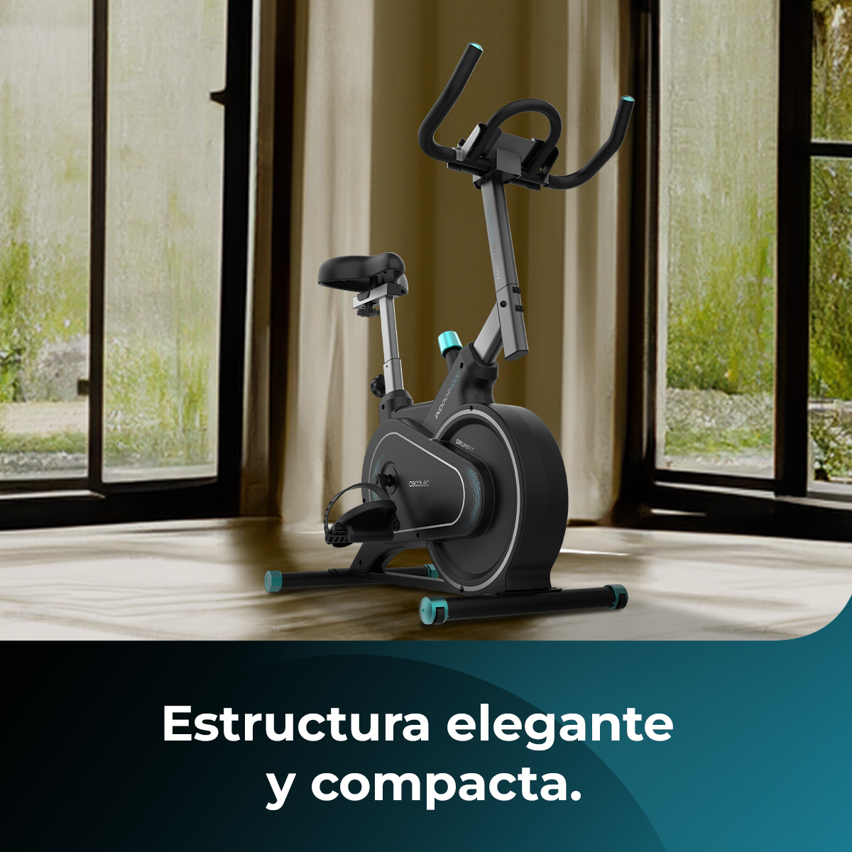 Una bicicleta estática está en una habitación. La bicicleta es negra y gris con detalles turquesas. Detrás de la bicicleta hay cortinas y una ventana.