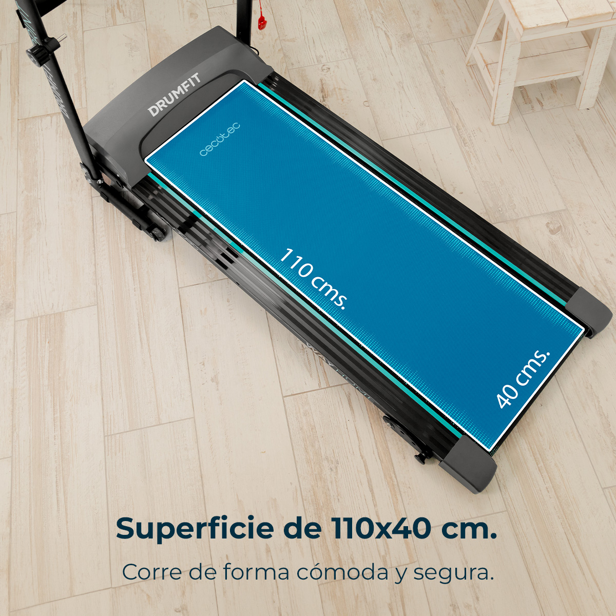 Bieżnia z niebieską powierzchnią do biegania, 110x40 cm, na jasnej drewnianej podłodze. Marka Drumfit, mały biały stołek.