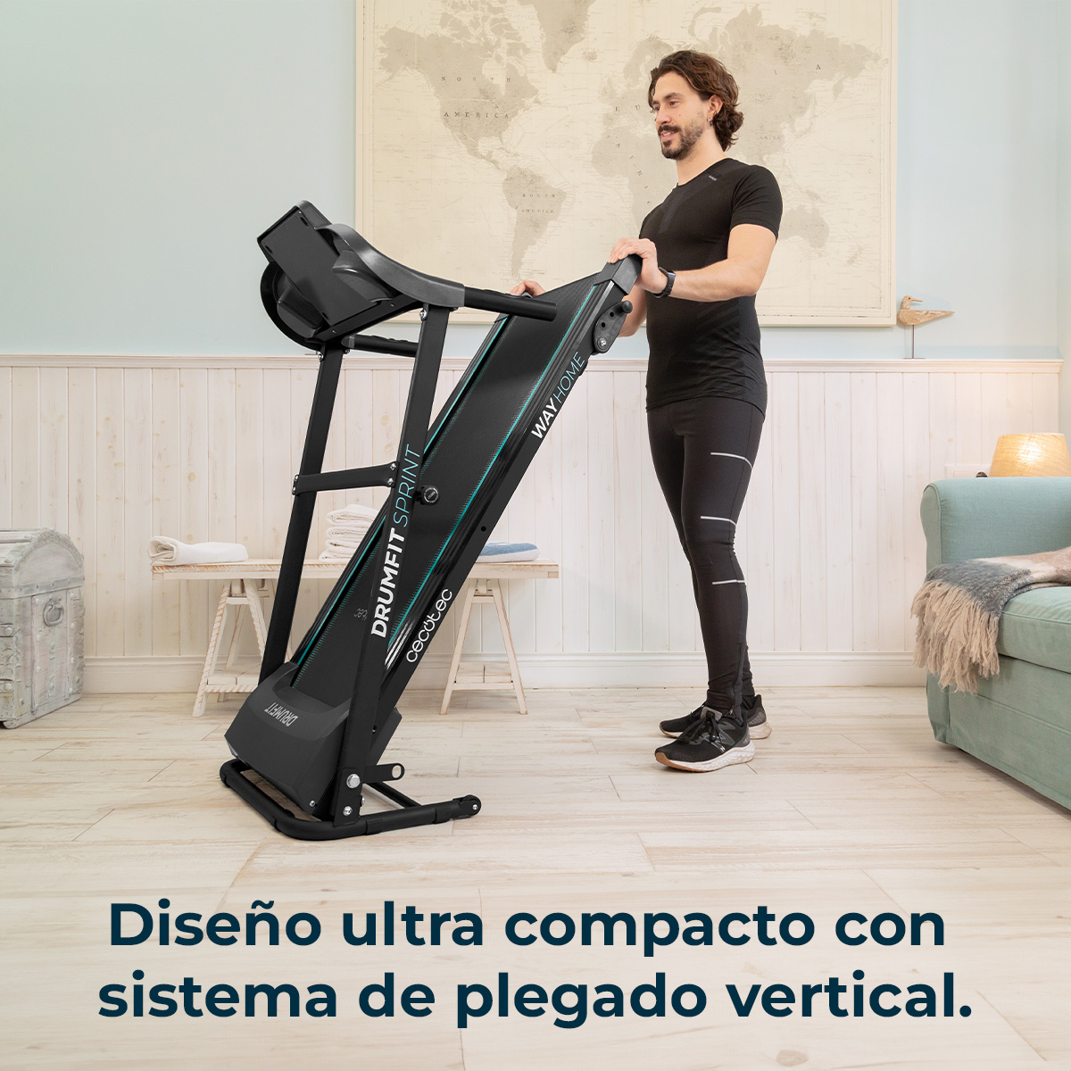 Mężczyzna stoi obok złożonej bieżni. Bieżnia jest czarna z zielonymi akcentami. Mapa wisi na ścianie.