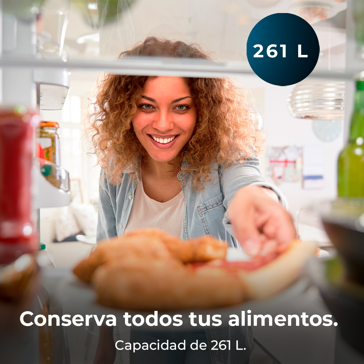 Una donna sorride, allungando la mano verso un frigorifero. All'interno, il cibo è visibile. Un'etichetta da 261 L è in alto.