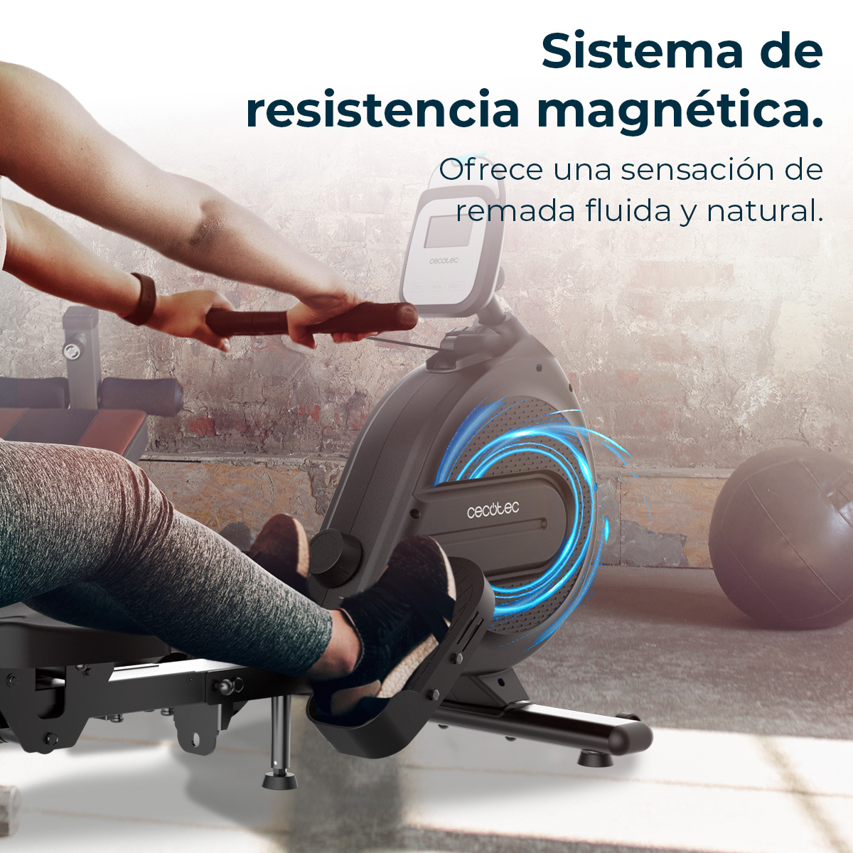 Una persona usa una máquina de remo. La máquina es negra con detalles azules. Una pelota medicinal gris en el fondo.