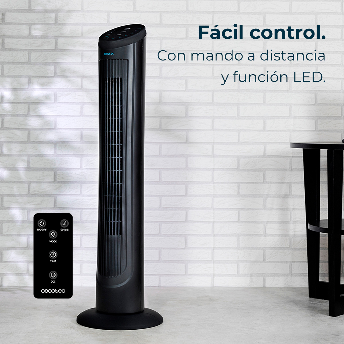Czarny wentylator wieżowy z pilotem na tle białej ceglanej ściany, mały stolik po prawej.