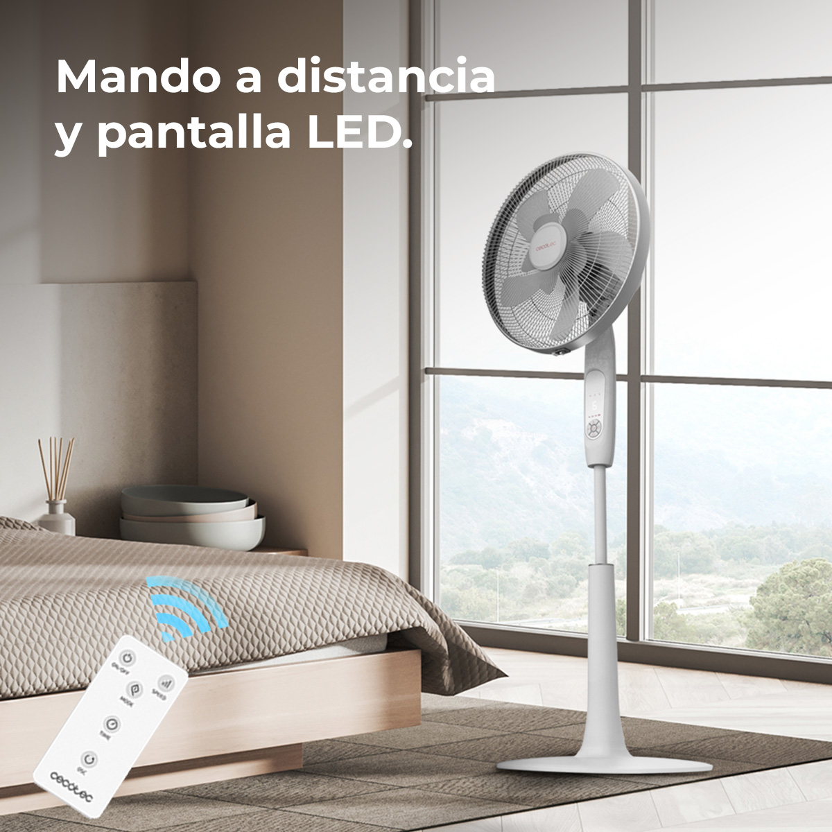 Biały wentylator stojący w pokoju. Pilot leży na łóżku. Wentylator stoi przy oknie z widokiem na góry.