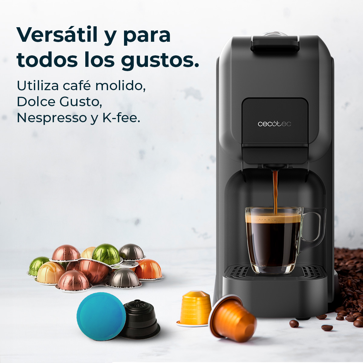 Una macchina da caffè nera sta preparando il caffè in una tazza di vetro. Capsule di caffè sono sparse. Testo: Versátil y para todos los gustos.