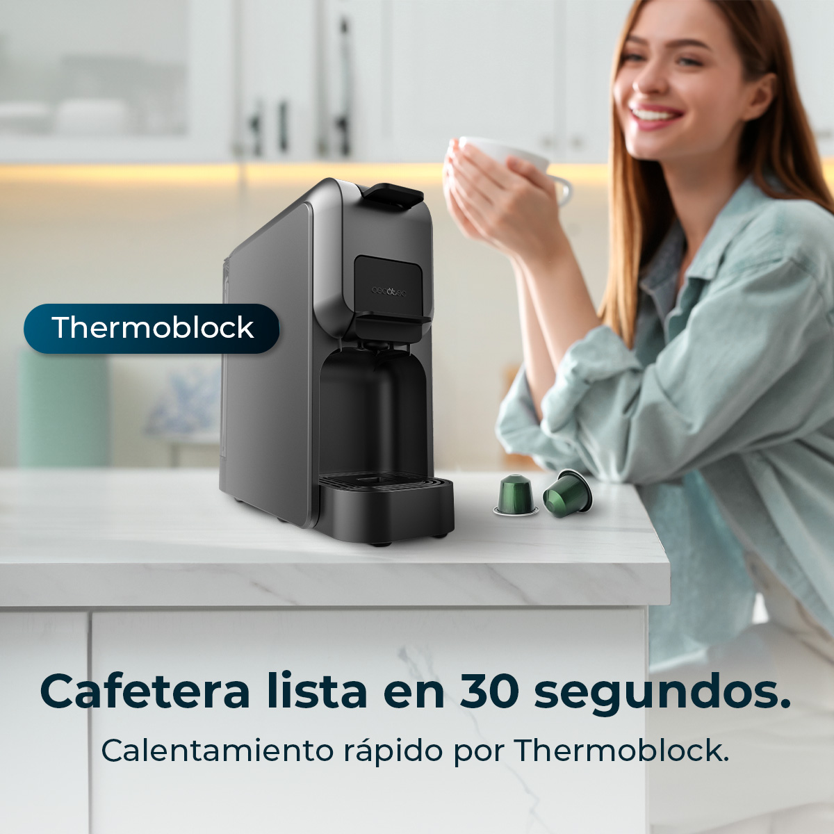 Una donna sorride tenendo una tazza. Una macchina da caffè nera con Thermoblock è sul bancone. Due capsule di caffè sono vicine.