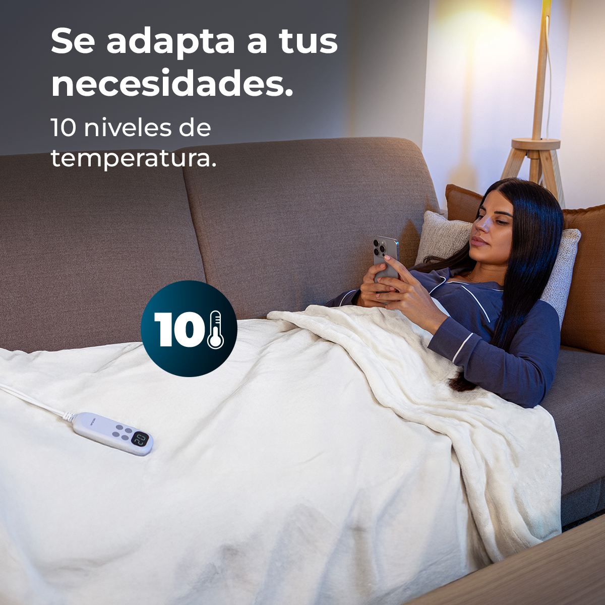 Una mujer está acostada en un sofá, usando un teléfono bajo una manta. El texto dice 'se adapta a tus necesidades' y '10 niveles de temperatura'.