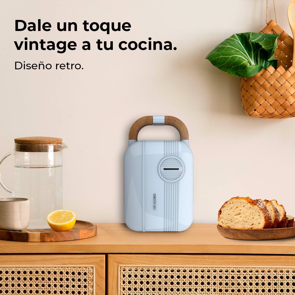 Un electrodoméstico retro azul claro con asa de madera está sobre una encimera de madera con pan, limón y una jarra de agua.