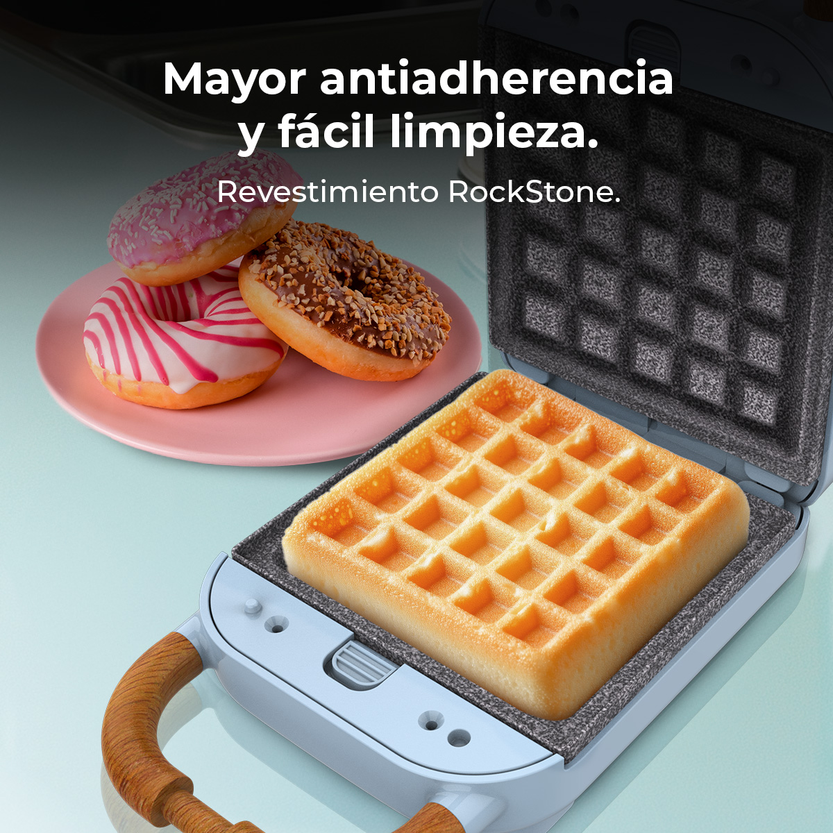 Una gofrera con un gofre cocido dentro y rosquillas en un plato en el fondo.