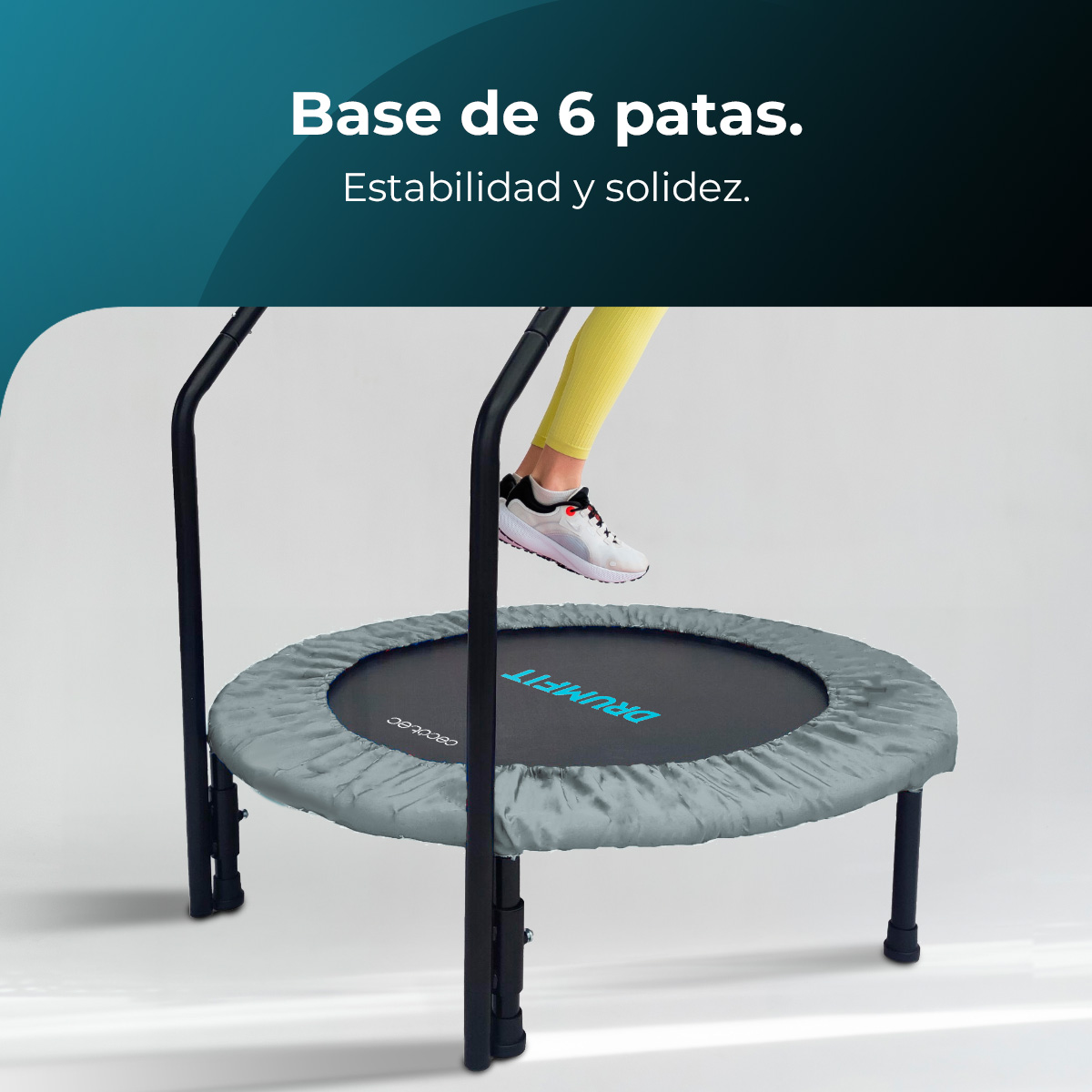 Osoba skacze na mini trampolinie. Ma szarą spódnicę, czarne nogi i czarne uchwyty. Osoba nosi żółte spodnie i białe buty.