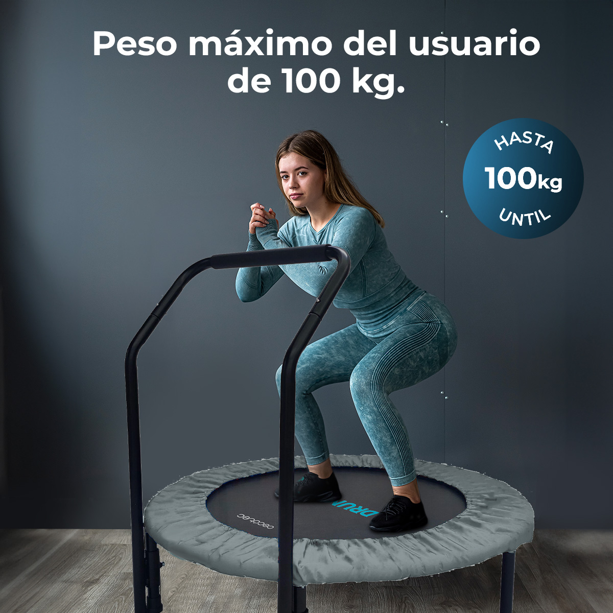 Kobieta kuca na trampolinie. Nosi niebieski strój sportowy. Znak mówi: 'Hasta 100kg Until'. Szare tło.
