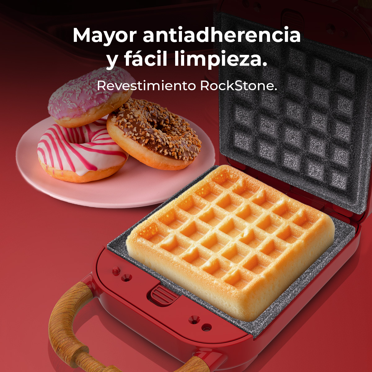 Una macchina per waffle rossa con un waffle cotto all'interno. Tre ciambelle su un piatto rosa sono sullo sfondo. Lo sfondo è rosso.