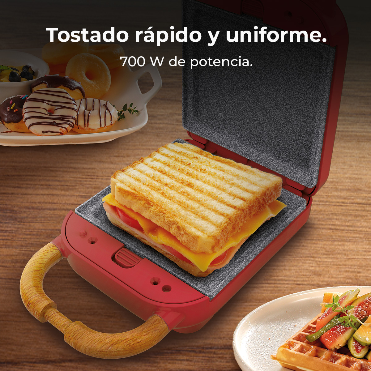Una sandwichera rossa con un sandwich grigliato all'interno. Ciambelle e waffle sullo sfondo.