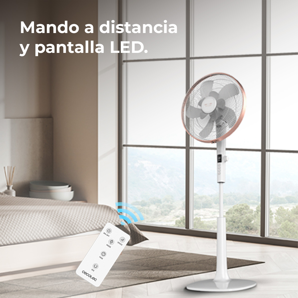 Un ventilatore bianco con anello oro rosa. Un telecomando in primo piano e un letto e una finestra sullo sfondo.