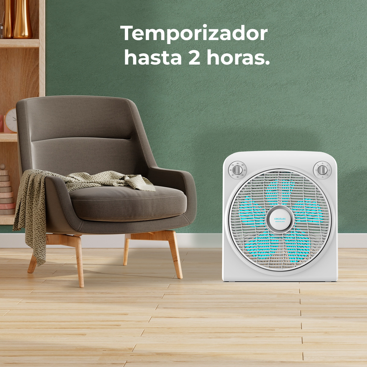 Biały wentylator z niebieskimi łopatkami po prawej stronie. Szary fotel z kocem po lewej. Zielona ściana w tle.