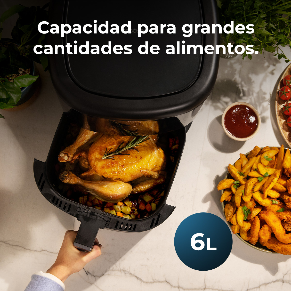 Een airfryer met een gebraden kip erin, naast friet, saus en tomaten. Een hand trekt de lade. De capaciteit is 6L.