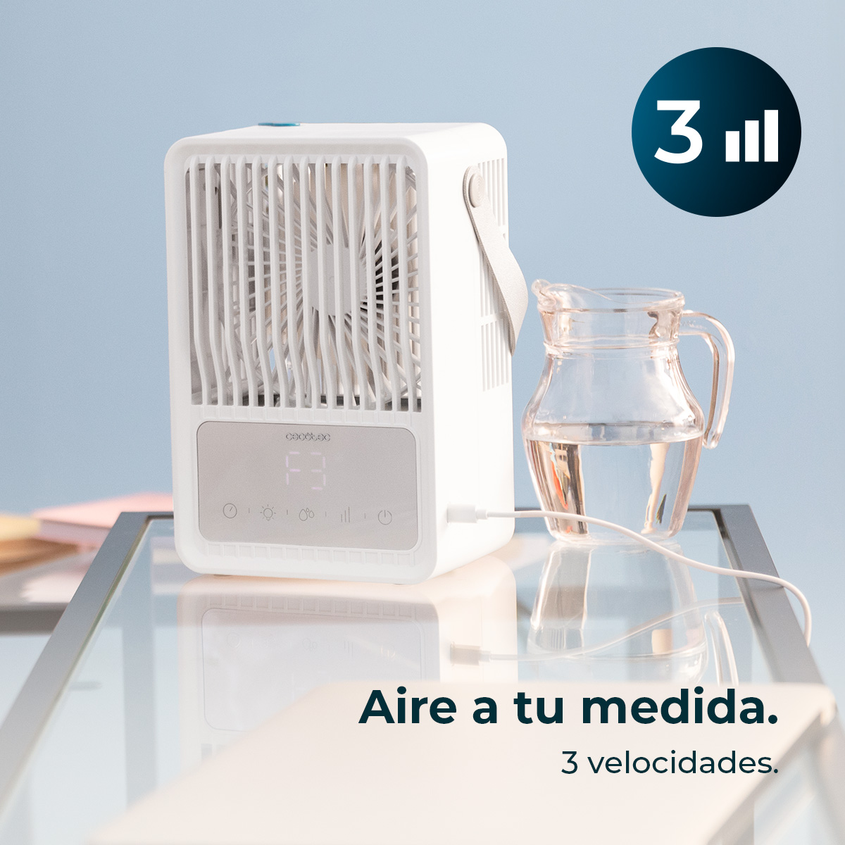 Condizionatore d'aria bianco vicino a una brocca di vetro con acqua. Il testo dice: 'Aire a tu medida. 3 velocidades'.