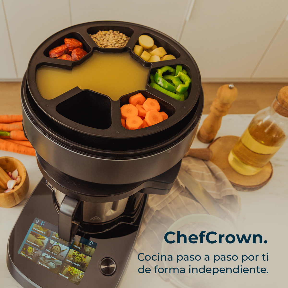Un procesador de alimentos con compartimentos llenos de ingredientes como zanahorias, pimientos y chorizo. También se ve una botella de aceite y texto.