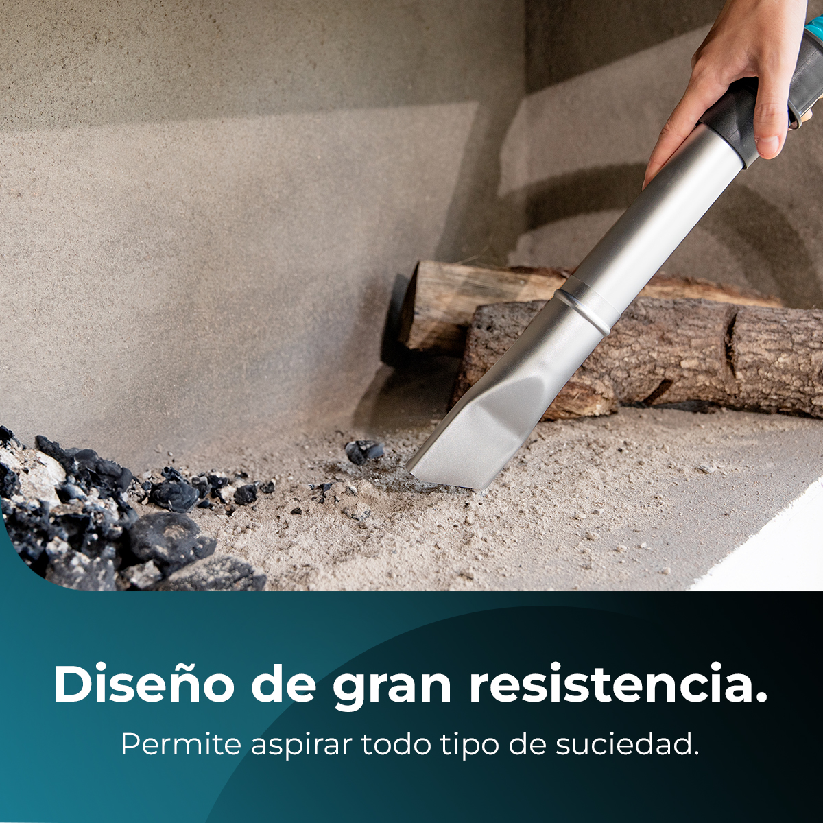 Una mano sostiene una boquilla de aspiradora sobre cenizas y arena. En el fondo, hay troncos y una pared de piedra.