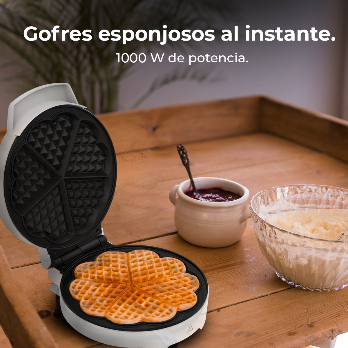 Una macchina per waffle con un waffle cotto. Accanto, una ciotola di pastella e un vasetto di marmellata, tutto su un vassoio di legno.