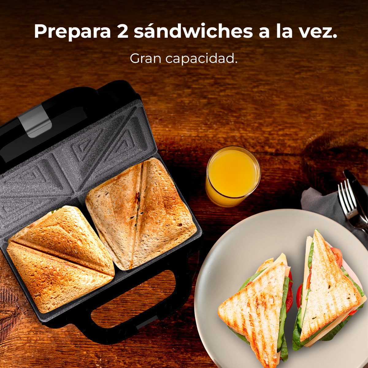 Una sandwichera con dos sándwiches dentro y dos listos en un plato. También se ve un vaso de zumo y cubiertos.