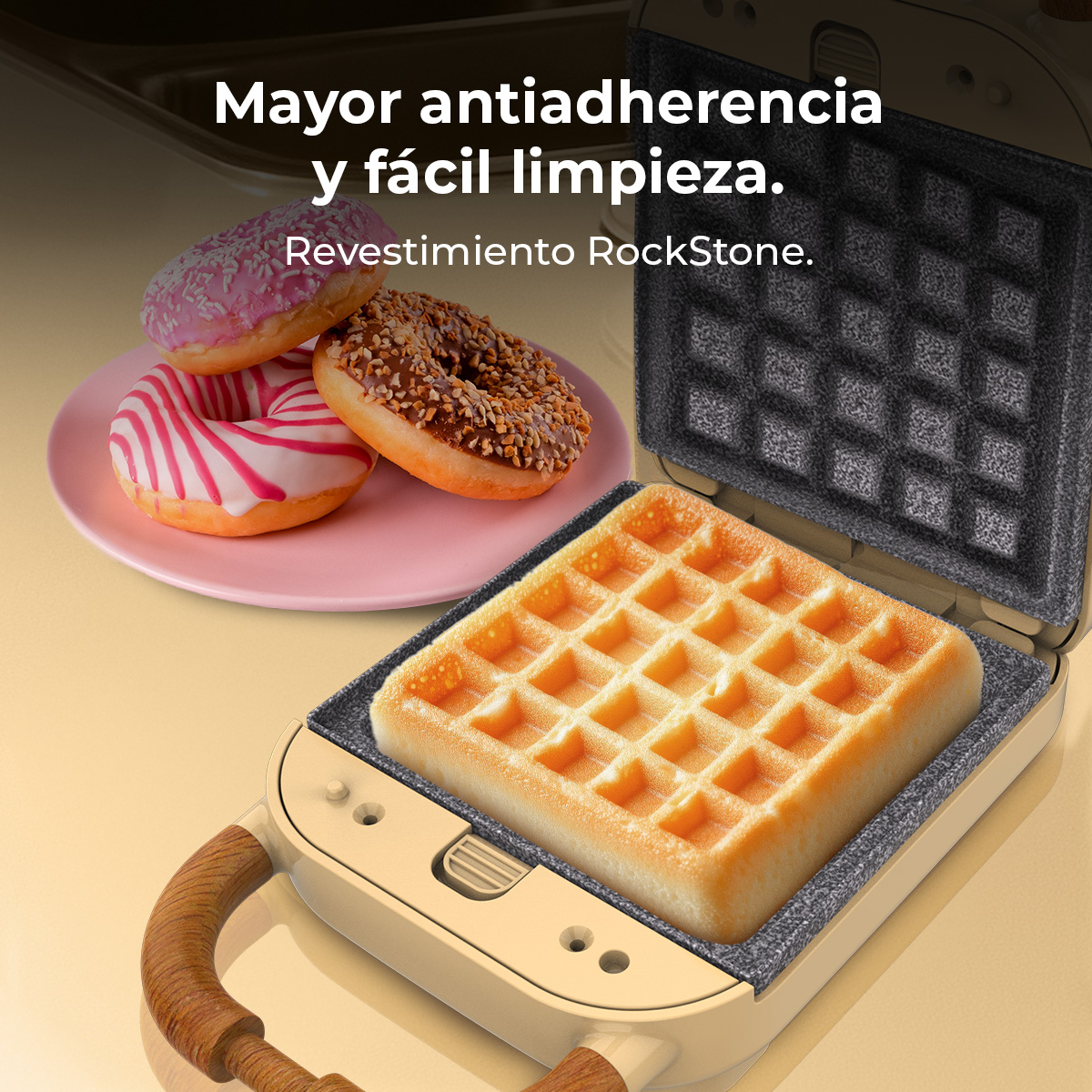 Una gofrera con un gofre cocinado dentro y rosquillas en un plato rosa. El texto de arriba dice 'Mayor antiadherencia y fácil limpieza'.