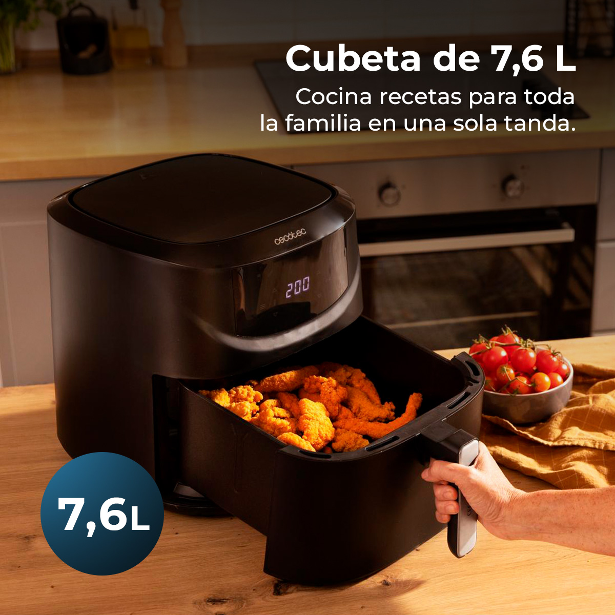 Een zwarte airfryer met eten erin, een kom tomaten en een hand die de handgreep vasthoudt. Tekst zegt '7,6L' en 'cecotec'.