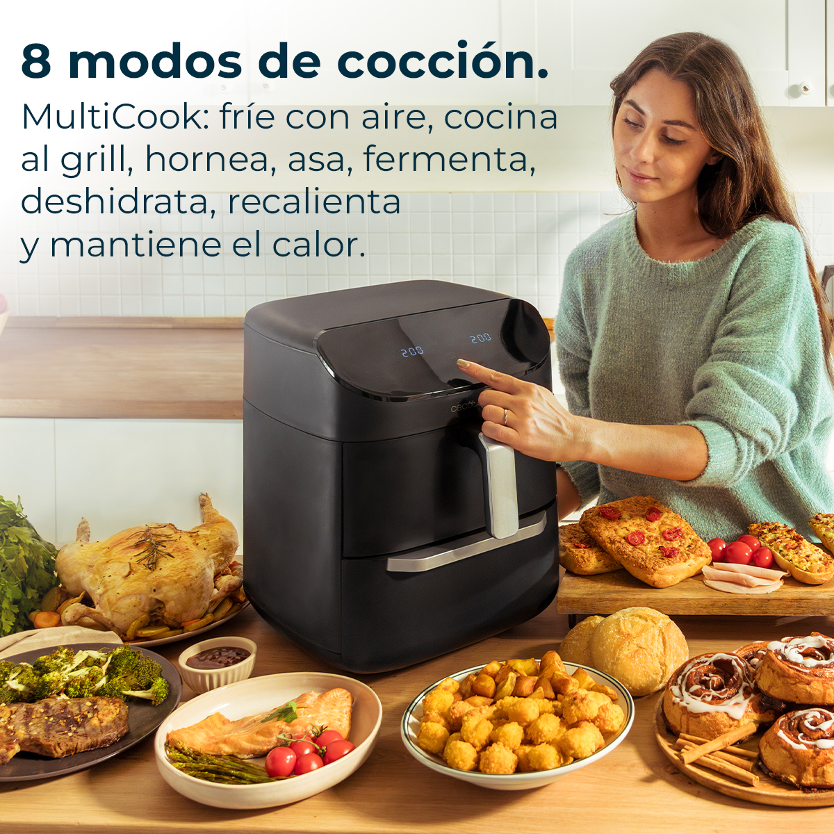 Kobieta obsługuje czarną frytkownicę powietrzną. Różne ugotowane potrawy, takie jak kurczak, warzywa i ciasta, znajdują się na stole przed nią.