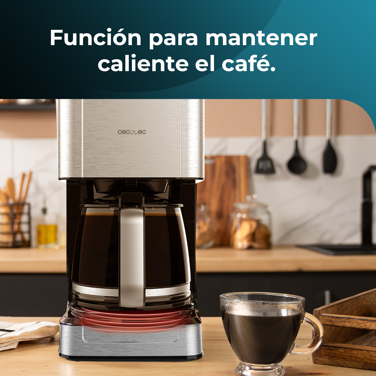 Una macchina da caffè con una caraffa di vetro piena di caffè è su un bancone di legno. Una tazza di caffè e utensili da cucina sono visibili.