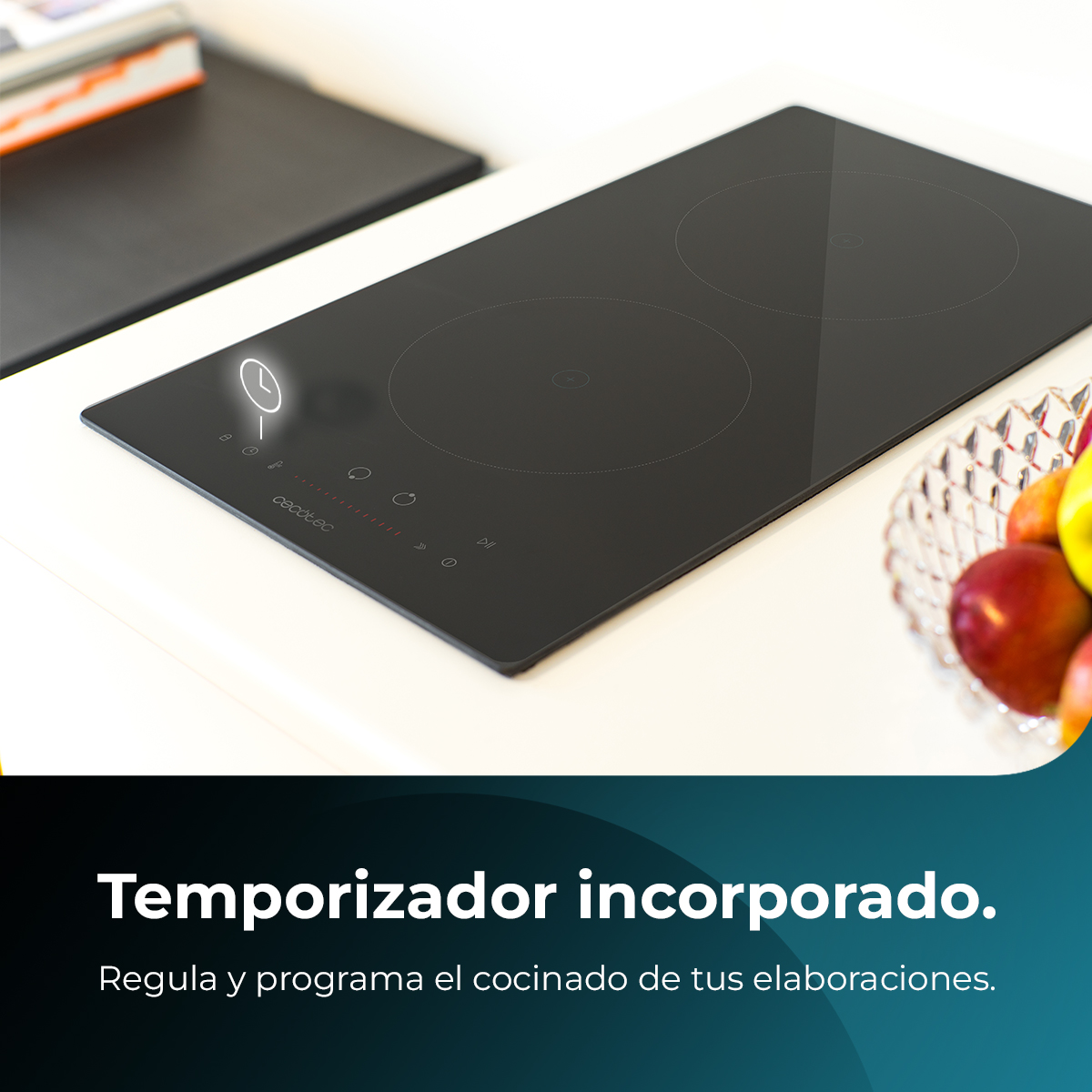 Un piano cottura a induzione nero con due fuochi. Una ciotola di frutta è a destra. Un libro è a sinistra.