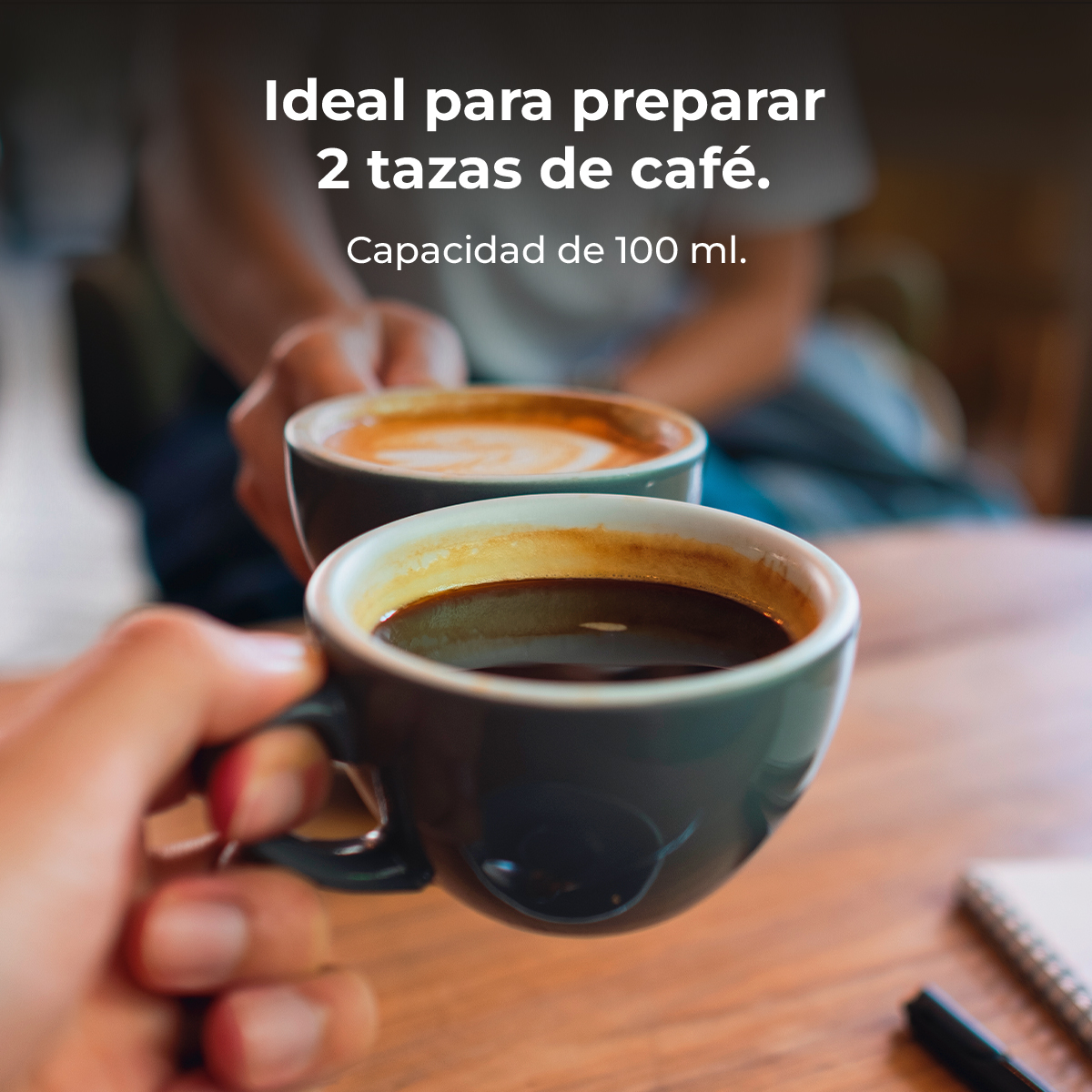 Dos manos sosteniendo tazas de café. Una con café negro, la otra con un latte color crema. El fondo está borroso.