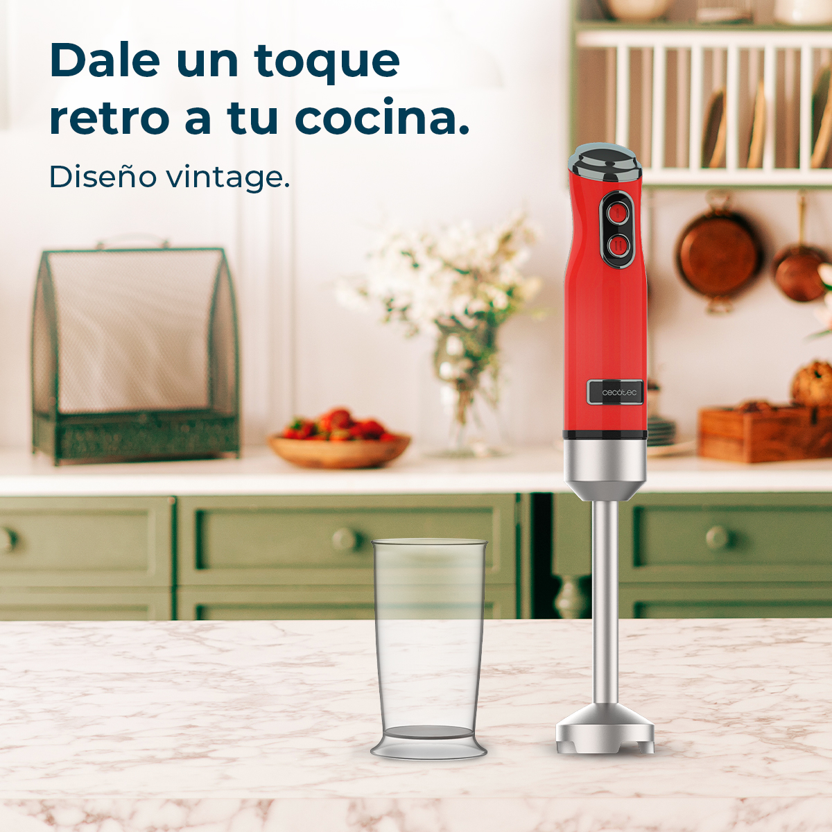 Un frullatore a immersione rosso è su un piano di lavoro in marmo. Accanto c'è un bicchiere. Sullo sfondo, una cucina con frutta e fiori.