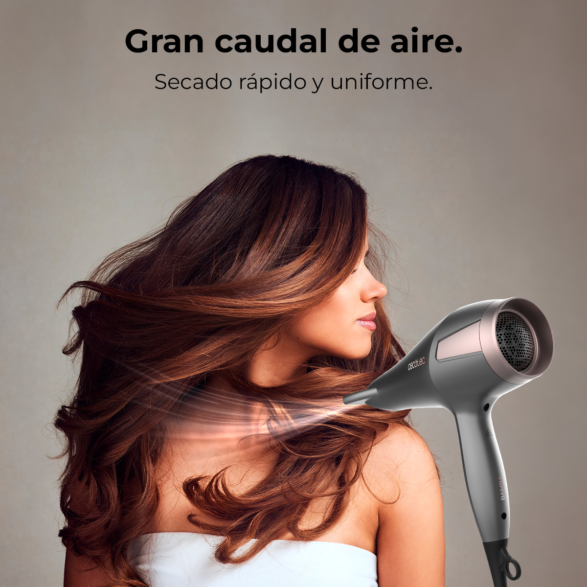 Una mujer con cabello castaño suelto se lo está secando con un secador de pelo gris y oro rosa.