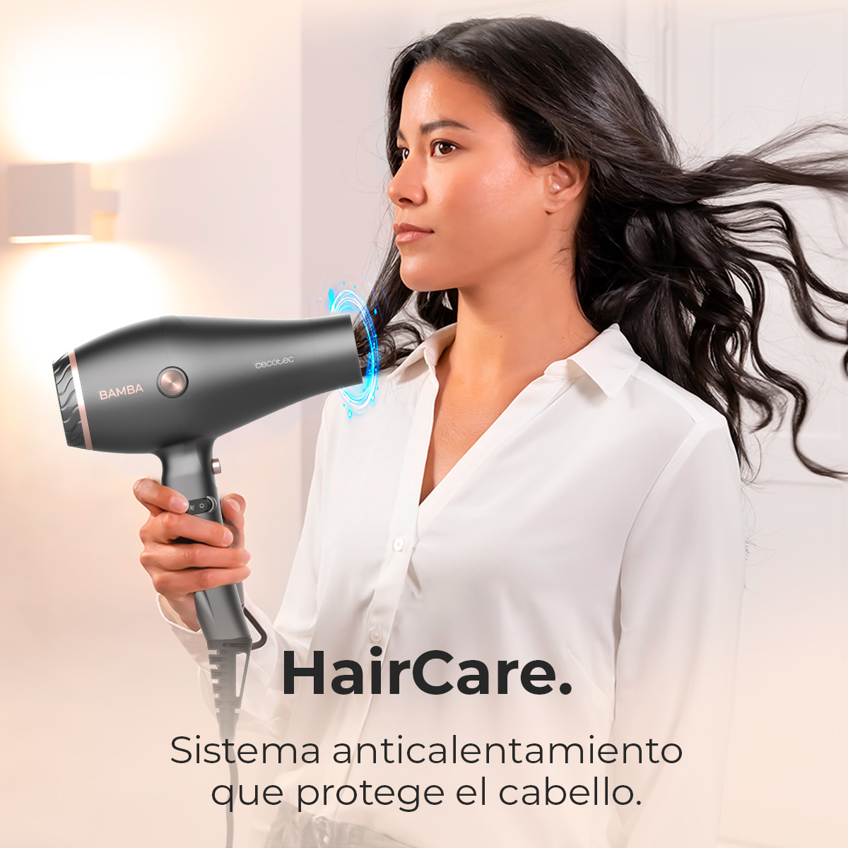 Una donna tiene in mano un asciugacapelli grigio scuro. Ha lunghi capelli scuri e indossa una camicia bianca. L'asciugacapelli ha dettagli oro rosa.