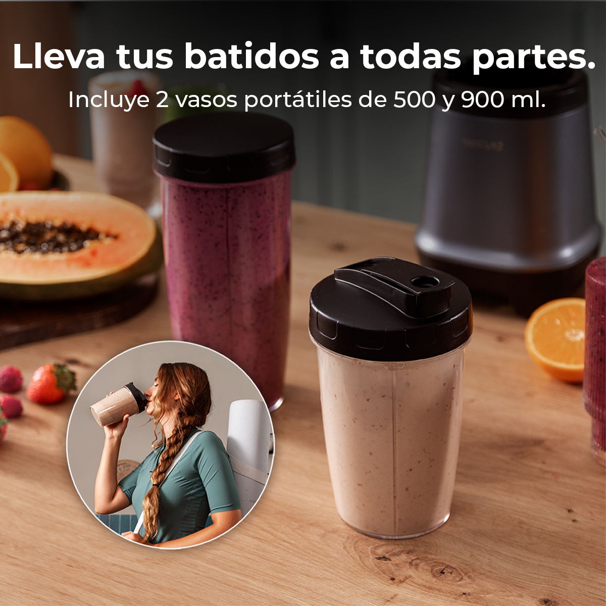 Imagen muestra vasos portátiles para batidos y una licuadora. Una mujer bebe de un vaso. Frutas en la mesa de madera.