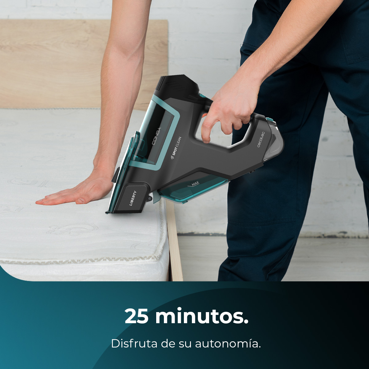 Una persona usa una aspiradora de mano sobre un colchón. La aspiradora es negra y turquesa. El fondo incluye una pared de madera y texto.