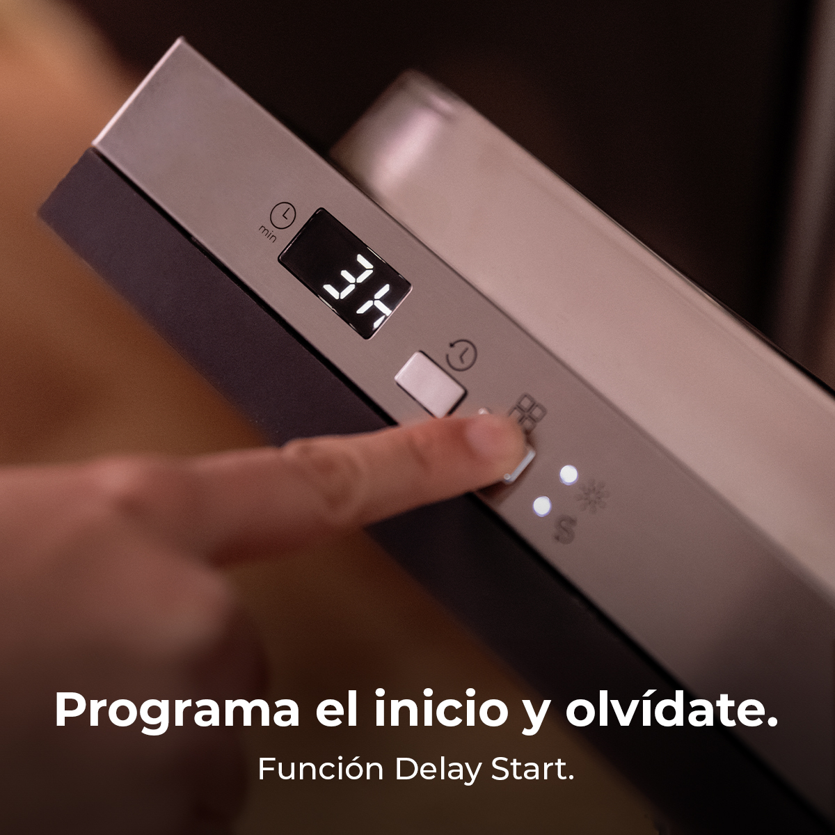 Ręka naciska przycisk na zmywarce. Na wyświetlaczu widać '34'. Tekst poniżej mówi 'Programa el inicio y olvídate'.