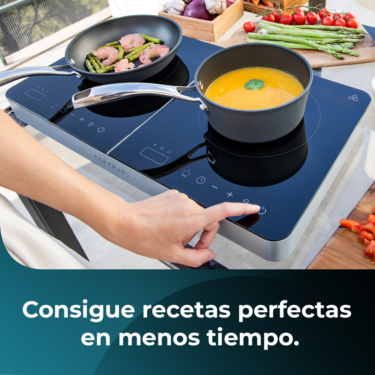 Ręka naciska przycisk zasilania na czarnej płycie kuchennej. Na płycie znajdują się patelnie z jedzeniem i warzywami na drewnianej desce.