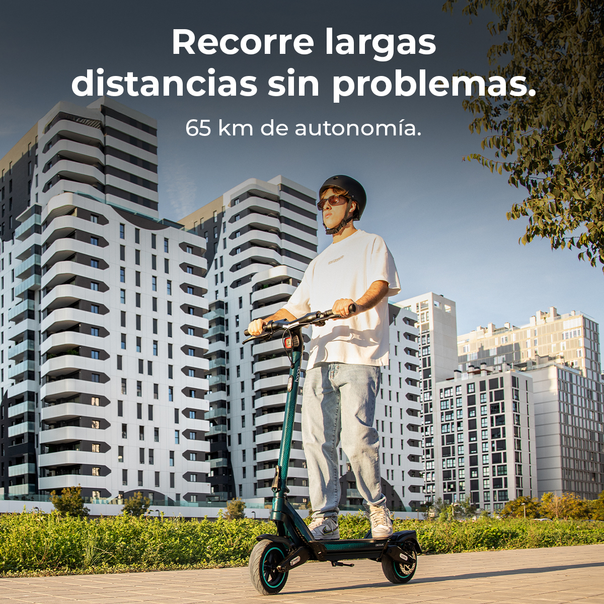 Un hombre monta en un patinete eléctrico sobre una acera. Hay edificios altos en el fondo. El texto dice: Recorre largas distancias sin problemas.