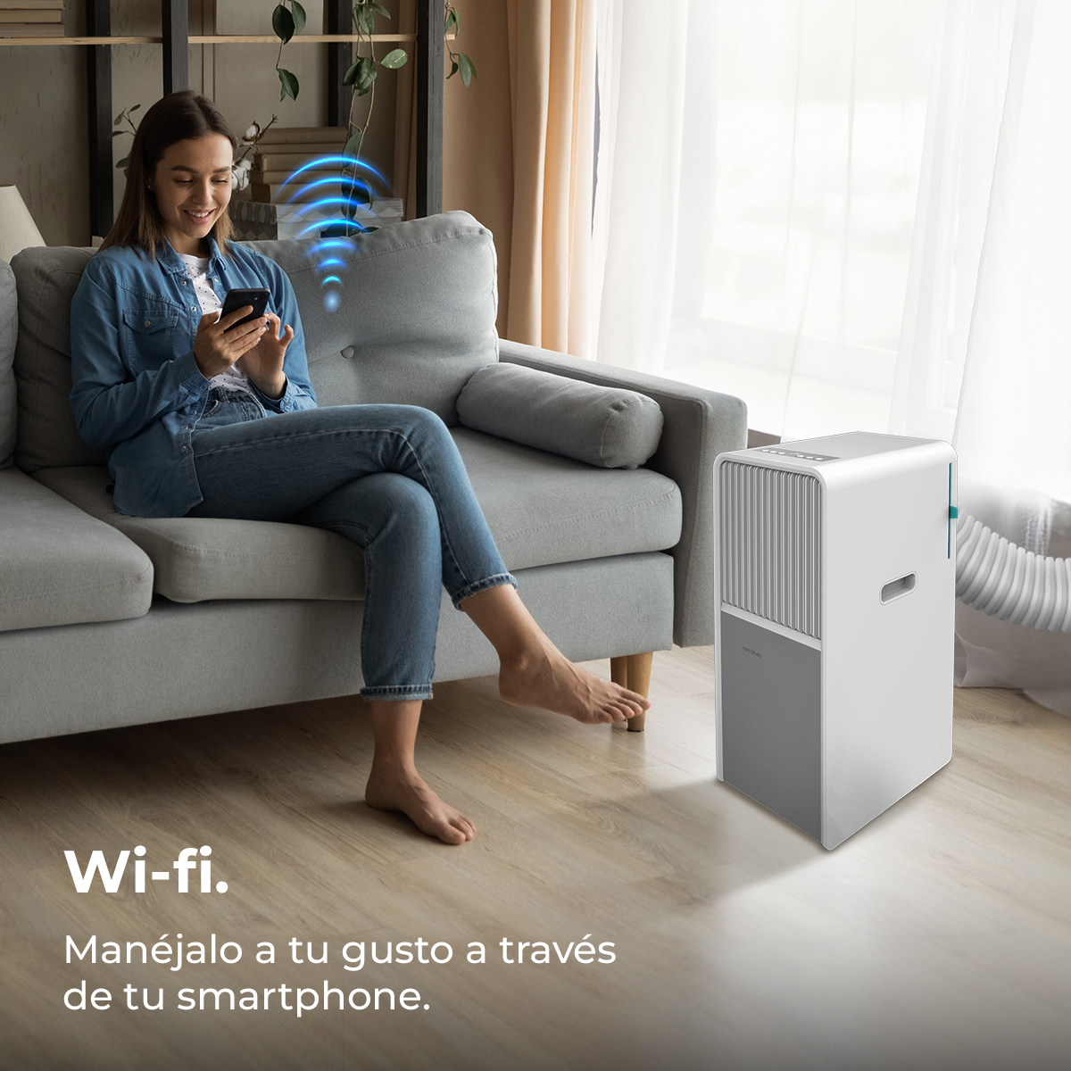 Kobieta na kanapie z smartfonem, symbol Wi-Fi. Biały klimatyzator po prawej. Tekst: Zarządzaj według upodobań przez smartfon.