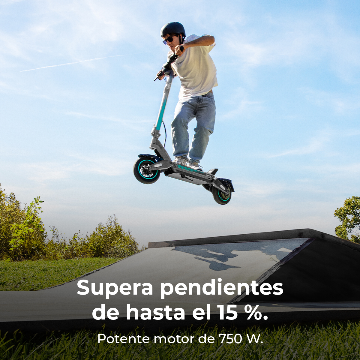 Un hombre con casco en un patinete eléctrico salta en el aire. Cielo azul, hierba verde y una rampa al fondo.