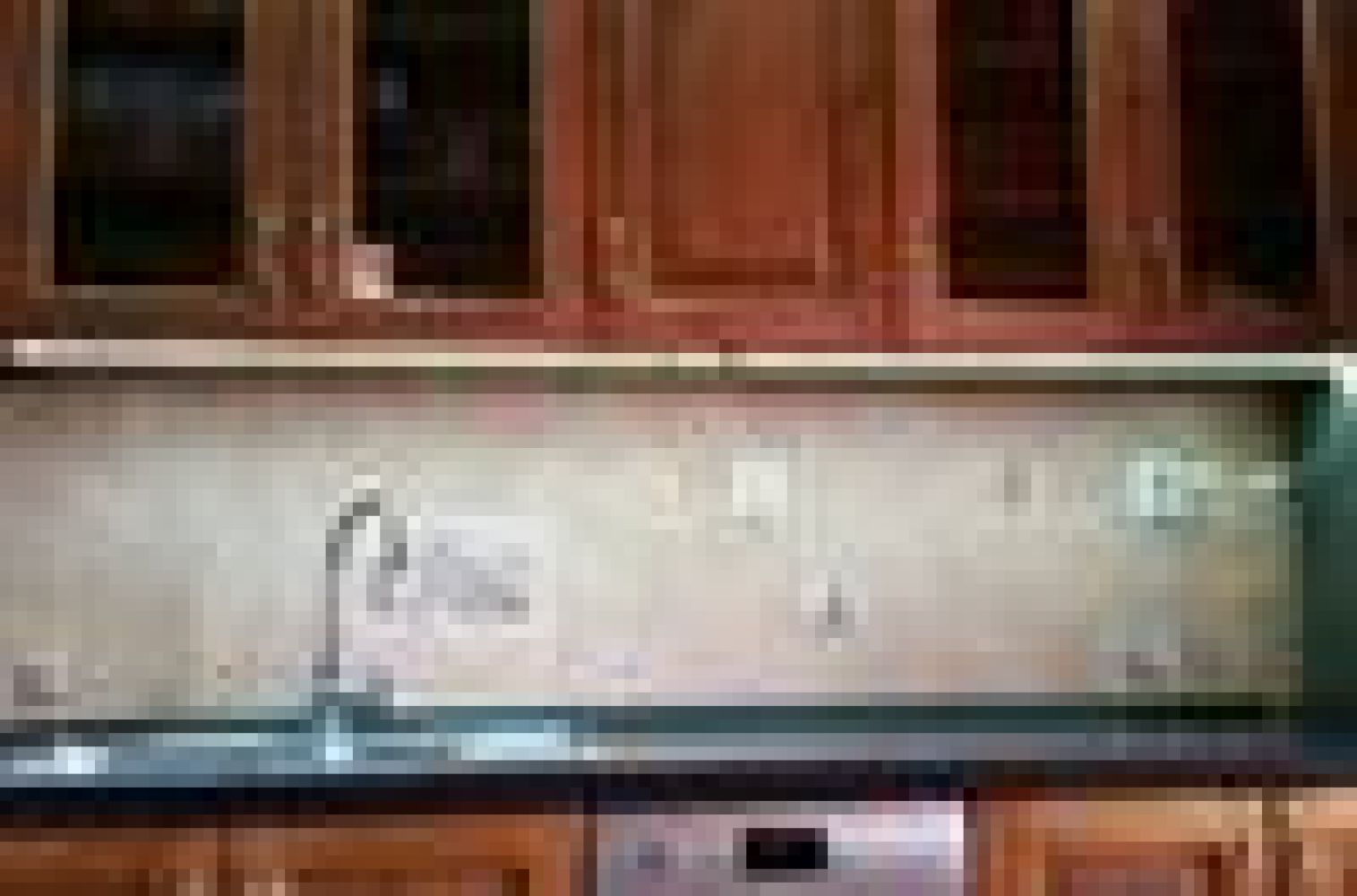 Kücheninterieur mit Holzschränken, einem Waschbecken und einem Geschirrspüler. Spritzschutz und Arbeitsplatten sind sichtbar. Deckenbeleuchtung.