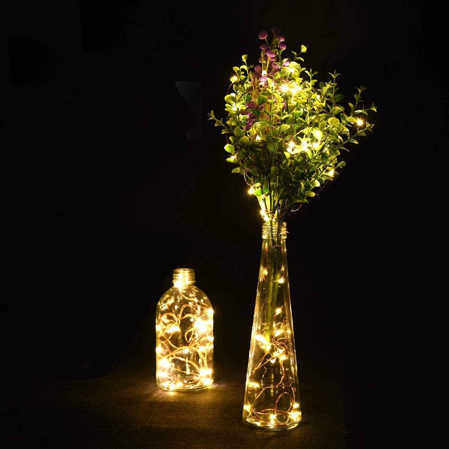 Zwei Glasvasen mit Lichterketten. Eine enthält Blätter und Blumen, die andere Lichter. Dunkler Hintergrund.